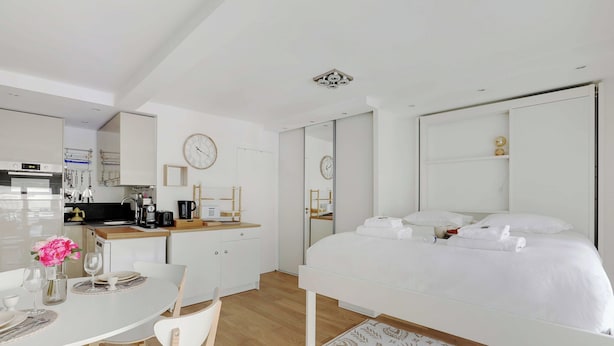 A modern hotel room with a large bed, a separate dining area with a white table and chairs, a kitchen area with a coffee machine, and a large mirror. - Cozy Studio - 2P - Place de la Bourse (Paris)
