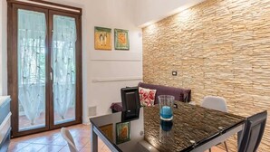 A dining area with a glass table, chairs, a stone wall, and a sofa with cushions.