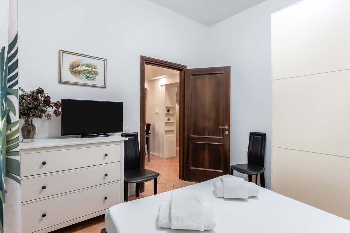 Een slaapkamer met een bed, een televisie op een dressoir, een deur en een stoel.