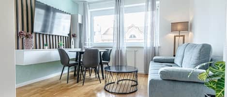 A modern living room with a grey sofa, a round coffee table, and a dining area with chairs and a table.