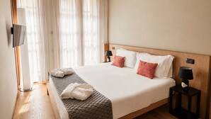 A hotel room with a large bed, two bedside tables, a TV, and a window with sheer curtains. - Cordigero - Riverside Suite (Peschiera del Garda)