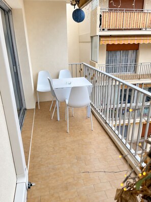 A balcony with a table and chairs, a railing, and a view of the building's interior.