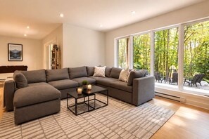A modern living room with a sectional sofa, a coffee table, and a view of a garden through large windows.