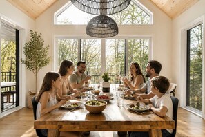 A family dining at a wooden table with large windows and a hanging light fixture. - BOREA Chalet | Spa, Golf & Outdoor Activities (Mont-Blanc)