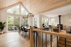 A spacious room with a wooden ceiling, large windows, a dining area with chairs, and a fireplace. - BOREA Chalet | Spa, Golf & Outdoor Activities (Mont-Blanc)