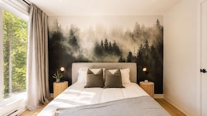 Una camera da letto con un letto grande, due comodini con lampade, un murale raffigurante una foresta e una finestra con tende.