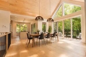 A spacious dining area with a wooden table and chairs, large windows, and a view of greenery. - BOREA Chalet | Spa, Golf & Outdoor Activities (Mont-Blanc)