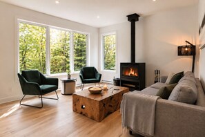 A modern living room with a fireplace, two green armchairs, a wooden coffee table, and a sofa.