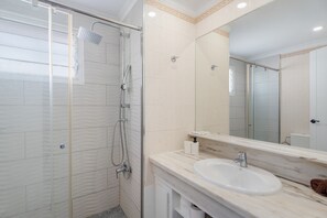 A modern bathroom with a glass-enclosed shower, a white sink, and a large mirror.