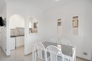 A modern kitchen with white cabinets, a tiled backsplash, and a dining area with a glass table and white chairs.