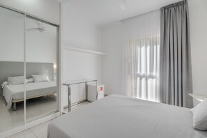A modern hotel room with a large bed, a glass partition wall, a small desk, and a window with curtains.