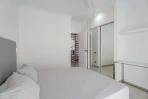 A bedroom with a bed, a glass table, a wardrobe, and a staircase leading to a bathroom.