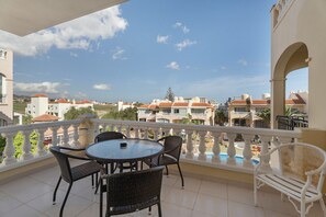 A balcony with a round table and chairs, a pool, and buildings in the background.