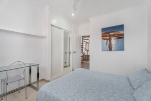A bedroom with a bed, a glass table, a chair, a wardrobe, and a painting on the wall.