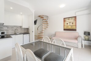 A modern kitchen with white cabinets, a microwave, and a dining area with a glass table and white chairs.