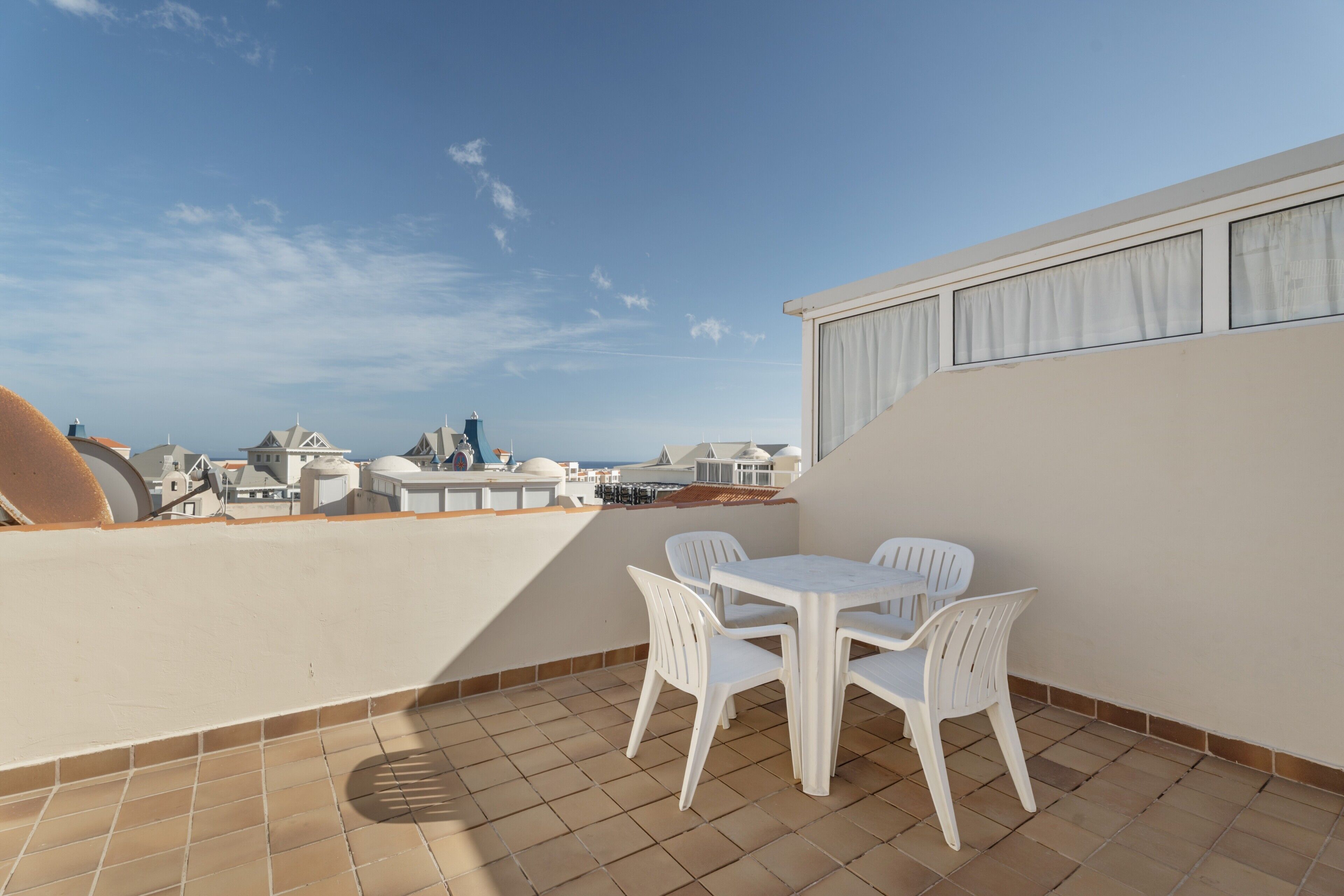 Eine Dachterrasse mit Tisch und Stühlen, Blick auf die Stadtlandschaft und ein Fliesenboden.