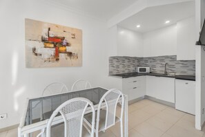 A modern kitchen with white cabinets, a microwave, and a dining area with a glass table and wicker chairs.