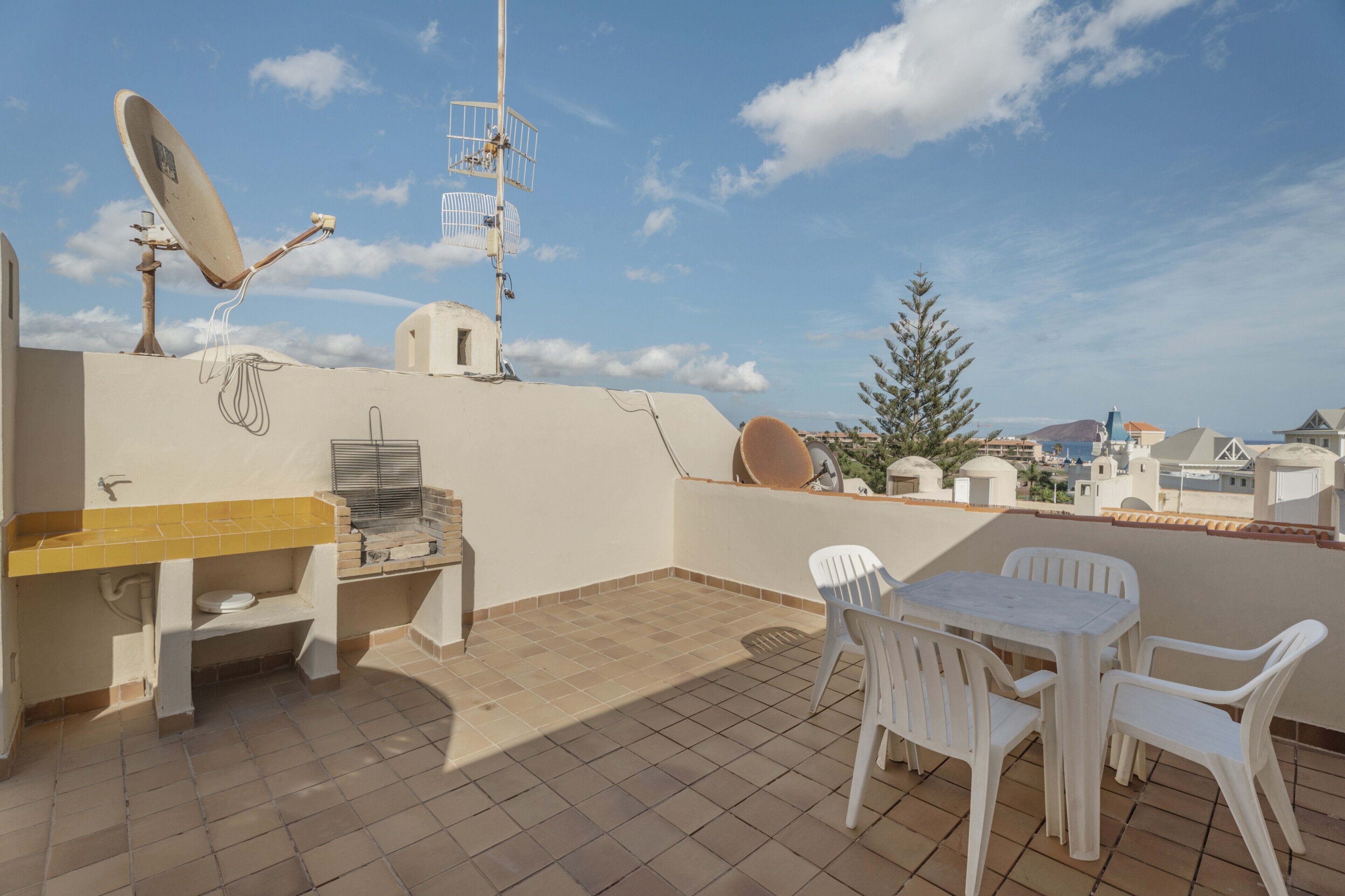 A rooftop terrace with a satellite dish, a small table with chairs, and a view of the cityscape.