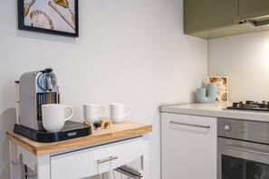 Een kitchenette met een koffieapparaat, twee witte mokken en een klein kastje.