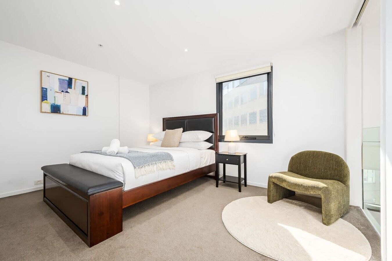 A modern bedroom with a bed, bedside tables, a chair, and a large window.