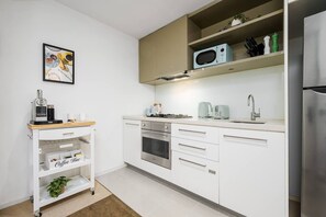 A modern kitchen with white cabinetry, a stainless steel refrigerator, a microwave, and a coffee machine. - Heritage Top Floor Loft CBD Parking (Melbourne)