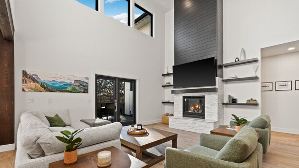 A spacious living room with a fireplace, a large TV, and a view of the outdoors. - Glacier Retreat Estates - Sweeping Mountain Views! (Columbia Falls)