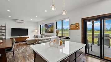 A modern living room with a large TV, a sofa, a dining area, and a kitchen island.