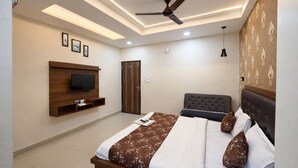 A bedroom with a bed, a TV mounted on the wall, a ceiling fan, and a door. - Hotel Shubhshree (Indore)