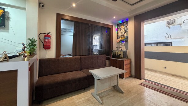 A modern living room with a sofa, a small table, a ceiling fan, and a fire extinguisher. - Hotel Shubhshree (Indore)