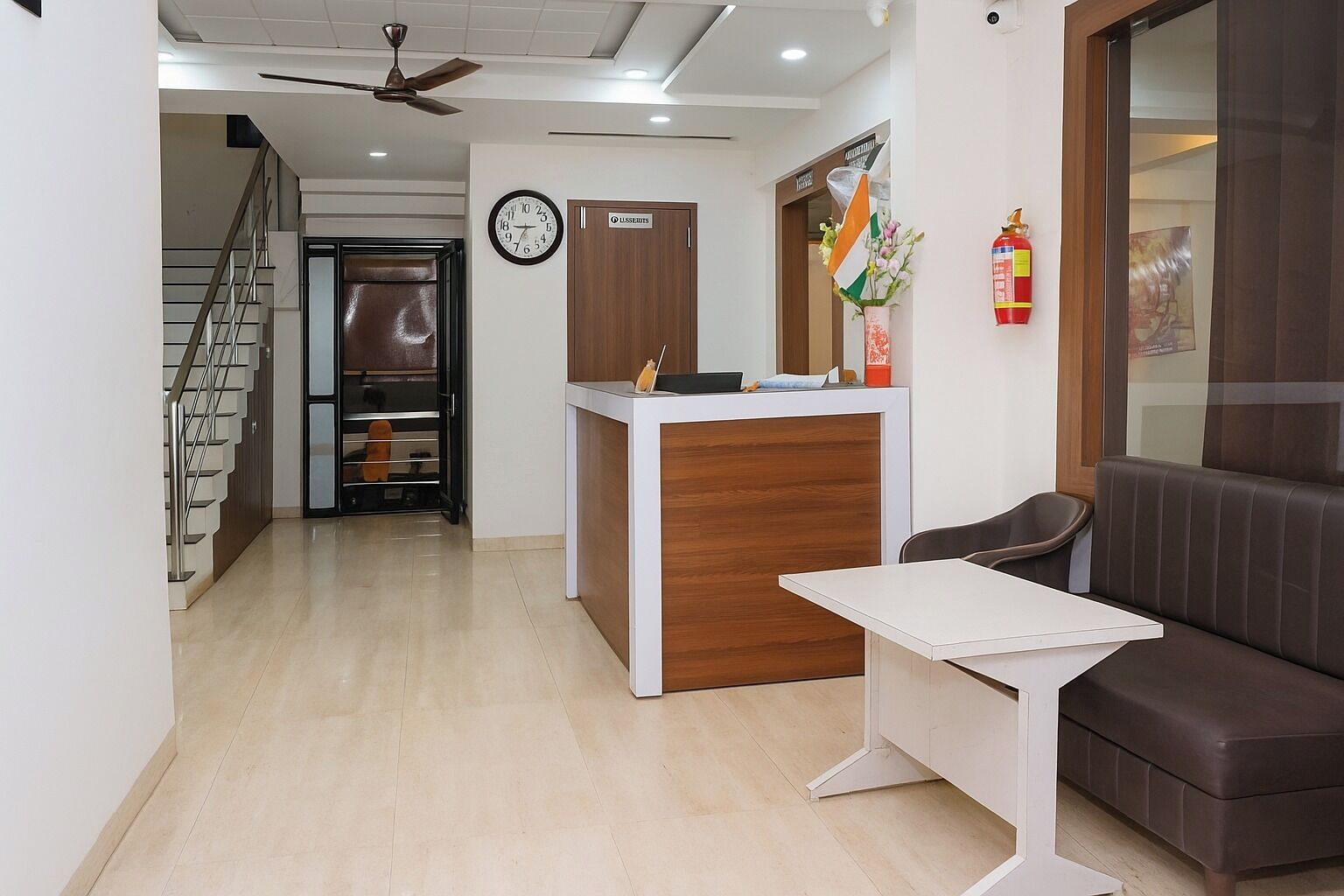 A reception area with a reception desk, a clock, a fire extinguisher, and a staircase.