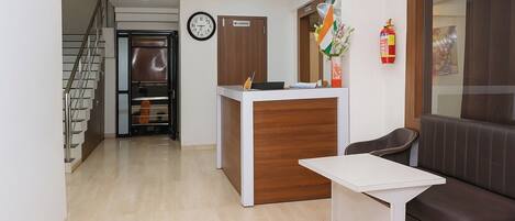 A reception area with a reception desk, a clock, a fire extinguisher, and a staircase.