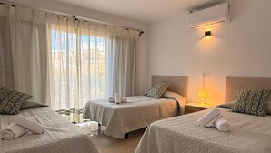 A hotel room with three beds, each with a white quilted bedspread and matching pillows. There is a window with sheer curtains, a bedside lamp, and an air conditioning unit mounted on the wall. - Marbella 22 Beach&Comfort just steps from the sea (Marbella)