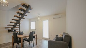 A modern living space with a wooden staircase, a dining area with chairs, a sofa, and a chandelier. - Sant'Avendrace: Spacious Apt. 3 bedrooms, 2 baths (Cagliari)