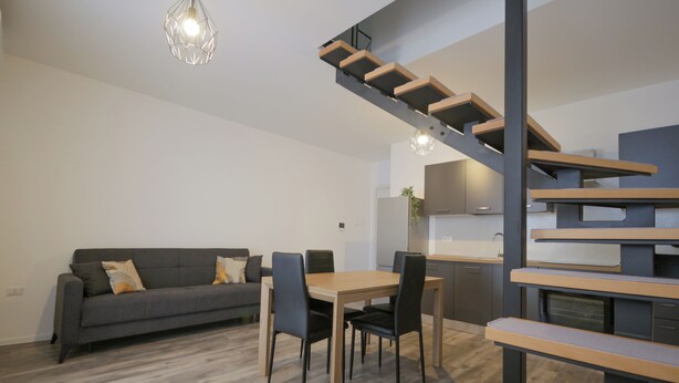 A modern living space with a dining area, a gray sofa, and a staircase. - Sant'Avendrace: Spacious Apt. 3 bedrooms, 2 baths (Cagliari)