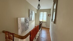 Una escalera con barandillas de madera y una manta roja, que lleva a una habitación con ventana y un candelabro.