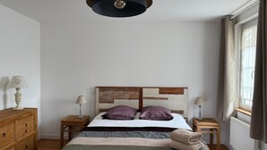 Un dormitorio con cabecera de madera, dos mesitas de noche con lámparas, un aparador de madera y una ventana con cortinas.