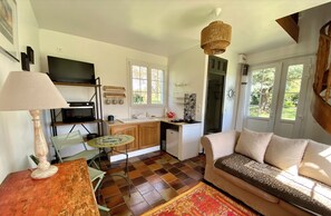 A cozy living room with a sofa, a coffee table, and a TV. There's a kitchen area with a stove, sink, and cabinets.