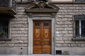 Une porte en bois à deux battants, dotée d’une poignée en laiton, flanquée de murs en pierre et ornée de rampes en métal ouvragé.