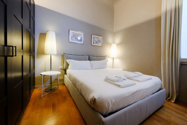 A hotel room with a large bed, two bedside lamps, a small round table, and two framed pictures on the wall.