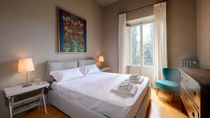 Une chambre à coucher bien rangée, avec un grand lit, des lampes de chevet, une fenêtre avec des rideaux et un tableau accroché au mur.