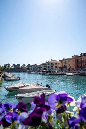 A canal with boats, buildings, and flowers. - Apartment 'Palazzo Cordigero - Bastioni' with Canal View, Wi-Fi and Air Conditioning (Peschiera del Garda)