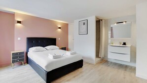 A modern bedroom with a bed, bedside tables, a nightstand, a bathroom with a sink and mirror, and a shower area. - Appartement in the Heart of Paris - Opera (Paris)