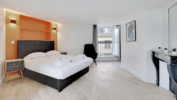 A modern hotel room with a large bed, a bedside table, a chair, a desk, and a balcony with a view. - Appartement in the Heart of Paris - Opera (Paris)