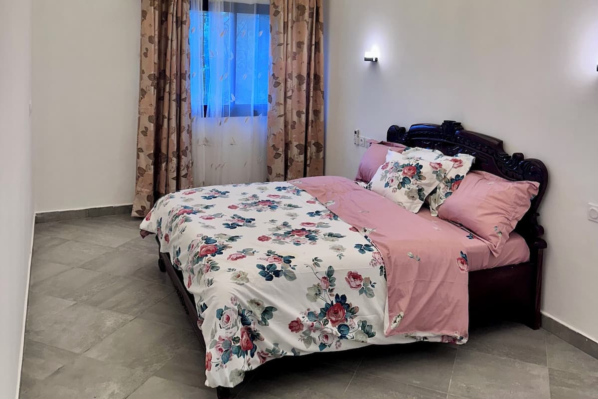 A bedroom with a bed, floral bedding, a ceiling with recessed lighting, and an air conditioning unit.