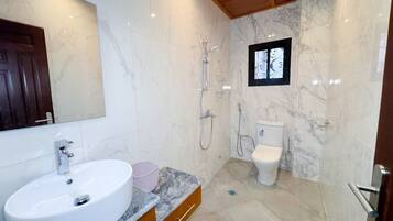 Un baño con lavamanos de mármol, inodoro y ducha.