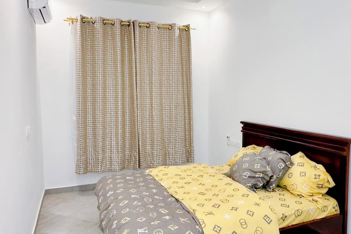 A bedroom with a bed, a wooden headboard, a patterned bedspread, and a curtain.