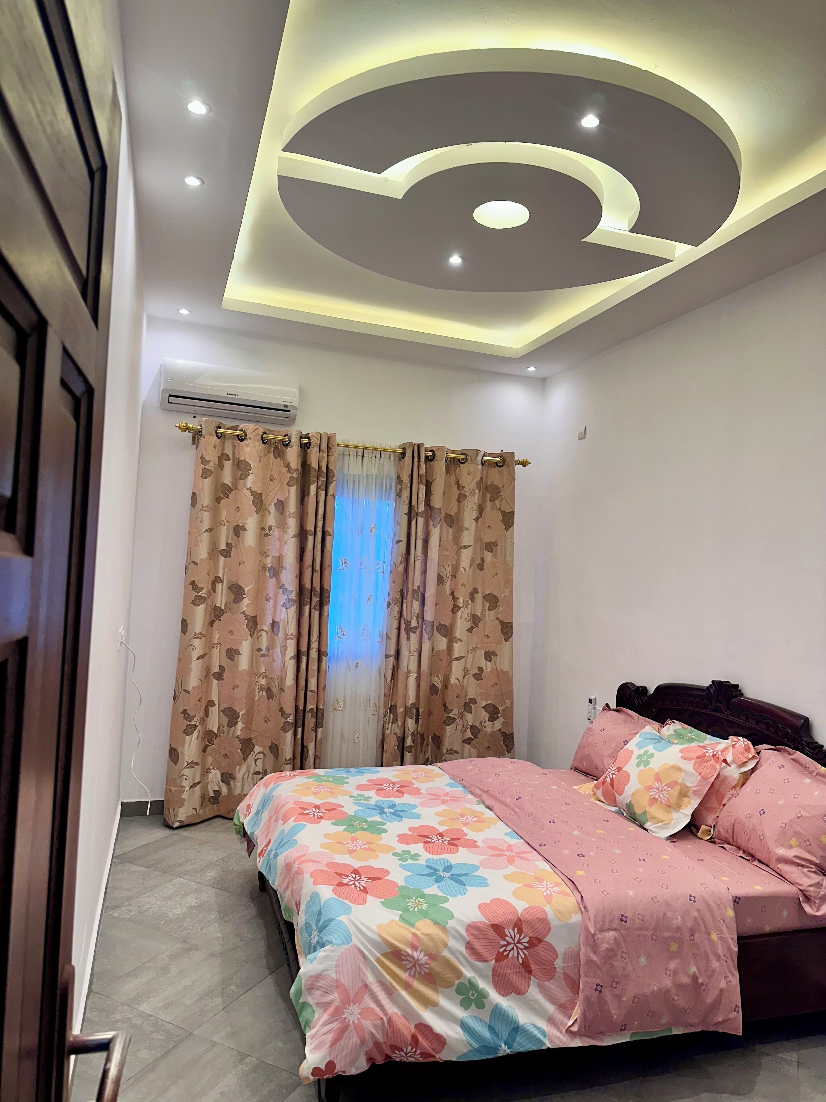 A bedroom with a bed, floral curtains, and a ceiling with recessed lighting.