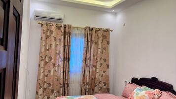 A bedroom with a bed, floral curtains, and a ceiling with recessed lighting.