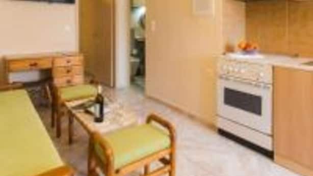 A compact kitchen with a dining area, wooden cabinets, a built-in oven, and a flat-screen TV. - Limonero New City Apartment 1 With Private Parking (Lefkada)