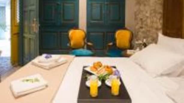 A hotel room with a bed, two chairs, a tray with food and drinks, and a stone wall. - Libretto Suites (Lefkada)